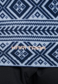Materiał polarowy w niebiesko-białym geometrycznym wzorze, z wyraźnym logo "KARI TRAA" w jasnoróżowym wykończeniu na środku.