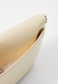 Pochette en tissu beige avec une texture lisse, une forme arrondie et une doublure douce visible à l'ouverture. Présente un éclat subtil.