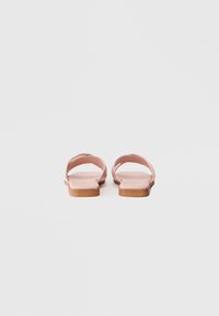 Pink flat sandals with two crossed straps and a textured insole, featuring a light brown rubber sole. Simple and minimalistic design.