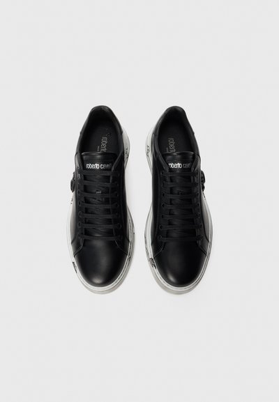 Black leather sneakers with black laces, white rubber soles, and subtle graphic accents. Features logo on tongue and unique stitching details.