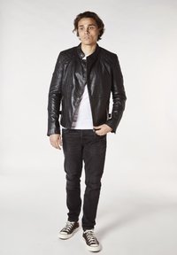 Svart skinnjacka med vadderade axeldetaljer, parat med en vit t-shirt, slitna svarta jeans och bruna högskor.