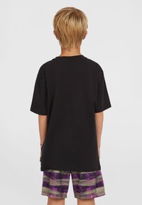 Camiseta de algodón negra de manga corta, combinada con pantalones cortos multicolores que presentan un patrón texturizado de rayas moradas, verdes y negras.