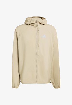 Veste à capuche beige avec zip intégral, fabriquée en tissu lisse ; elle présente des manches raglan et un logo Adidas réfléchissant sur la poitrine.