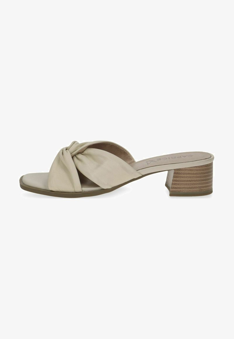 Beige heeled slide sandal with knotted front design, smooth leather material, open toe, and a block heel with a textured finish.