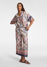 Gedrukte twee-delige outfit met een losse, korte mouwen top met een V-hals en wijde broek. Kleuren zijn blauw, roze en crème.