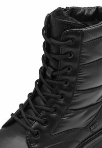 Czarne zimowe buty z górną częścią wykonaną z skóry i puchowego tekstylu, z okrągłymi sznurówkami, metalowymi oczkami i teksturowanym wzorem na cholewie.