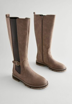 Rudos iki kelių batai su matinio paviršiaus apdaila, turintys šoninį užtrauktuką, elastingą panelę lankstumui ir tekstūruotą gumos pada.