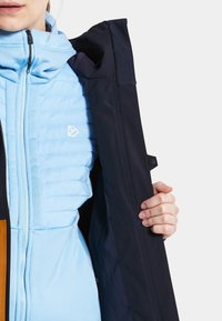 Light blue insulated jacket with a navy outer shell. Features quilted texture and a zipper. Logos visible on both layers.