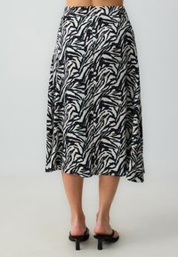 Schwarz-weiß bedruckter Rock mit einem Zebramuster. Fließendes, knielanges Design mit glatter Textur und seitlichem Schlitz für mehr Bewegungsfreiheit.