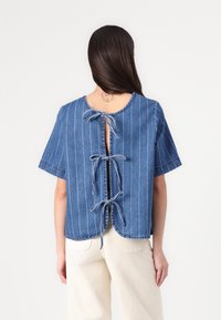 Top corto in denim blu a maniche corte con righe bianche verticali, scollatura rotonda e retro aperto con lacci regolabili.