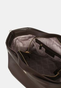 Borsa a tracolla in pelle marrone con chiusura a zip, dotata di una morbida fodera lavanda e diversi scomparti interni per l'organizzazione. Accenti in metallo dorato.