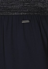Marine jurk met een gestructureerde zwart en zilveren bovenkant, met een geraffineerde taille en een metalen label met de tekst "DREIMASTER" aan de zijkant.