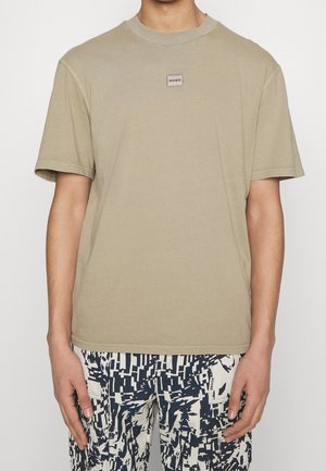 Kurzes T-Shirt mit kurzen Ärmeln und kleinem "HUGO"-Label auf der Brust, kombiniert mit weißen und schwarz abstrakt gemusterten Hosen.