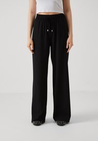 Pantalons larges noirs en tissu doux avec une taille élastique et un cordon de serrage. Texture lisse avec une coupe ample.
