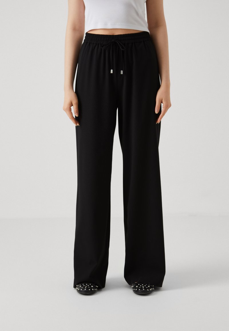 Pantalons larges noirs en tissu doux avec une taille élastique et un cordon de serrage. Texture lisse avec une coupe ample.