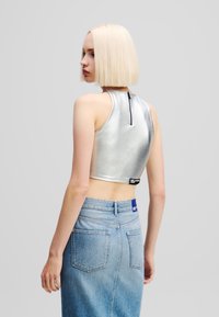 Srebrni metalni crop top s visokim izrezom, zatvaranje na patentni zatvarač na leđima, kombiniran s svijetlim traper suknjom olovka koja ima stražnje džepove.