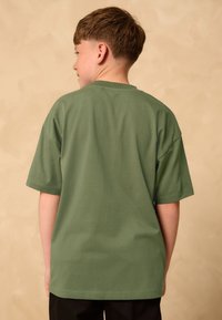 Zelena majica od pamuka s kratkim rukavima, okruglim izrezom i opuštenim krojem. Jednobojna tkanina bez istaknutih uzoraka ili ukrasa.