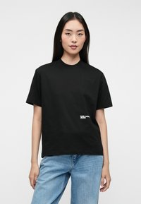Čierne bavlnené tričko s okrúhlym výstrihom a krátkymi rukávmi, so bielym logom "KARL LAGERFELD JEANS" na leme. V kombinácii s svetlo modrými džínsami.