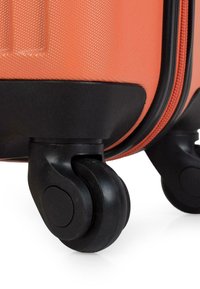 Maleta rígida naranja con superficie texturizada, base dura negra y ruedas negras lisas y pivotantes para una fácil movilidad.