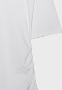 Vêtement blanc à manches courtes avec un détail de fronces sur le côté créant une texture de tissu froncée le long de la couture.
