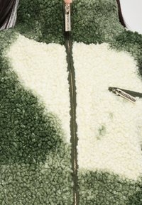 Jachetă din polar verde și galben, cu guler înalt, material texturat, închidere cu fermoar la jumătate și un buzunar pe piept cu fermoar.