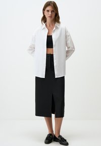 Chemise blanche à boutons, haut noir court, jupe midi noire avec fente latérale et mocassins noirs. Tissu lisse ; coupe ajustée ; design simple.