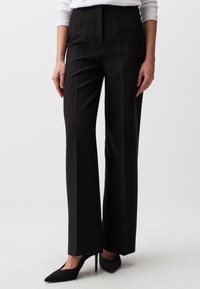 Zwarte pinstripe broek met een op maat gemaakte pasvorm, hoge taille en ruime benen, gecombineerd met puntige zwarte hakken. Soepele stofstructuur.