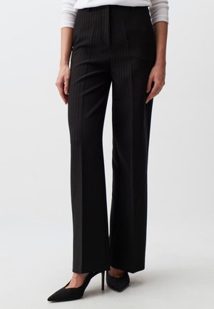 Pantalon noir à rayures, avec une coupe ajustée, taille haute et jambes larges, associé à des talons aiguilles noirs. Texture de tissu lisse.