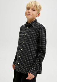 Melna un balta pārbaudītas krekli ar garām piedurknēm un klasisku apkakli. Iezīmē baltas pogas un brīvu piegriezumu.