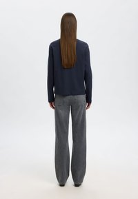 Tumesinise pikade varrukatega särk, mis on kombineeritud hallide laiade pükste ja klassikalise disainiga, sujuva tekstuuriga, vaadates seljalt.