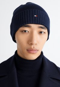 Bonnet en tricot côtelé bleu marine avec un petit logo. Fabriqué en fil doux, il offre un ajustement confortable et un motif texturé sur toute sa surface.