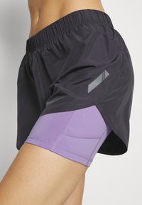 Mustat kevyet juoksushortsit, joissa on joustava vyötärö ja kerroksellinen muotoilu, sekä violettiset sisäshortsit. Include hienovarainen harmaa yksityiskohta.