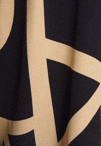 Tissu beige et noir avec un motif géométrique audacieux présentant de grandes formes qui se croisent et des plis doux.