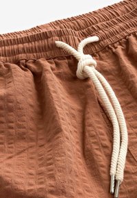 Shorts in tessuto marrone con texture, dotati di vita elastica e lacci. I lacci sono di colore crema con estremità in metallo.