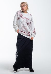 Hvid langærmet sweatshirt med burgundy fiskegrafik og "Ed Hardy" tekst, parret med en sort maxiskørt med broderede detaljer.