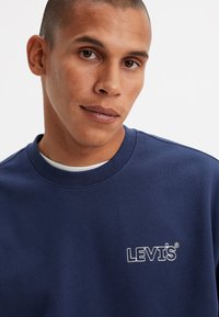 Felpa blu navy in cotone con scollatura a girocollo. Presenta un logo "LEVI'S" ricamato sul petto. Texture liscia.