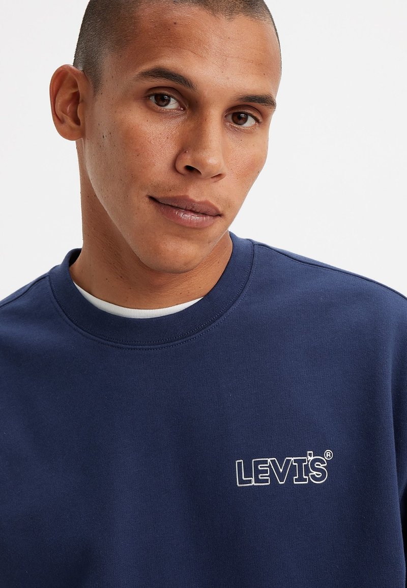 Granatowa bluza z bawełny z okrągłym dekoltem. Posiada białe haftowane logo "LEVI'S" na piersi. Gładka faktura.