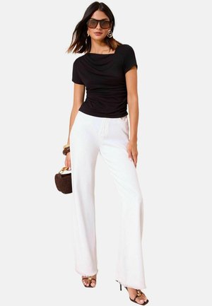 Top corto nero con dettagli drappeggiati, abbinato a pantaloni bianchi a gamba larga. Gli accessori includono occhiali da sole oversize e una piccola borsa marrone.