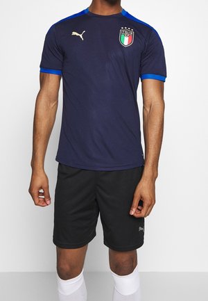 Marinblå Puma-fotbollströja med blå accenter, gulddetaljer och Italiens emblem. Kombinerad med svarta shorts och vita strumpor.