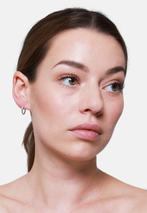Boucle d'oreille en argent sterling sur un modèle. La boucle est fine, circulaire et polie, mettant en valeur les teintes de peau naturelles et un maquillage simple.