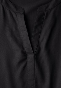 Haut en tissu noir avec un décolleté en V et des détails de couture subtils, offrant une texture lisse et un design simple.