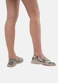 Instap schoenen met een gestructureerde slangenprint in zwart en beige, voorzien van een flexibele zool en een laag profiel ontwerp.