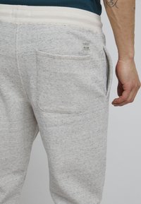Joggers de textura gris claro con cinturilla elástica blanca y un bolsillo trasero; presenta una pequeña etiqueta de la marca en el bolsillo.