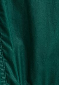 Κοντινό πλάνο σκουρό πράσινου υφάσματος με ορατή ραφή και πτυχώσεις.