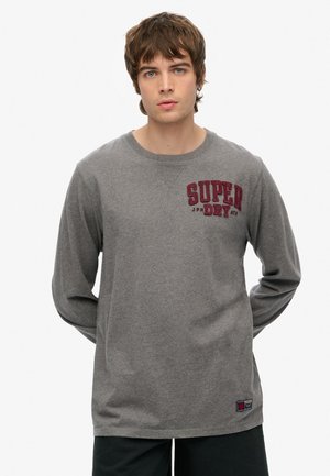 Camiseta de manga larga gris hecha de algodón, con un gráfico rojo impreso "SUPER DRY" en el pecho y un pequeño parche de logo en el dobladillo.