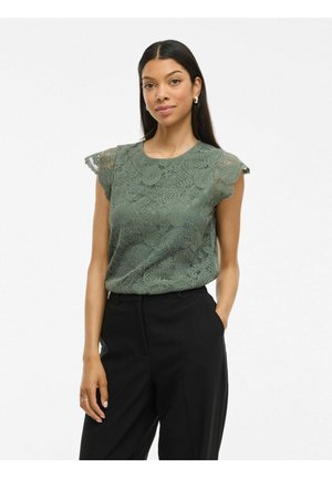 Top in pizzo verde muschio con maniche corte e volant. Presenta dettagli floreali intricati e un collo rotondo. Abbinato a pantaloni neri.