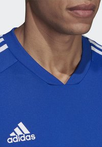 Blaues Sporttrikot mit V-Ausschnitt, aus glattem Material gefertigt. Besitzt weiße Streifen an den Schultern und ein weißes Adidas-Logo auf der Brust.