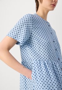 Abito blu con maniche corte, caratterizzato da pois navy, scollo rotondo e vita arricciata con tasche.
