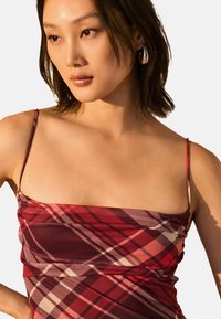 Robe à carreaux rouges avec des fines bretelles ; présente une coupe ajustée et un design froncé. Le motif comprend des nuances de bordeaux et de pêche.