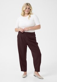 Burgundy high-waisted trousers with front pleats, tailored fit, smooth texture. Paired with a fitted white top and beige flats.
